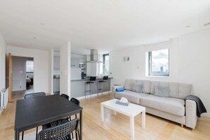Ein modernes Wohnzimmer mit einer Couch, einem Esstisch mit Stühlen, einer Küchenzeile und einem großen Fenster.