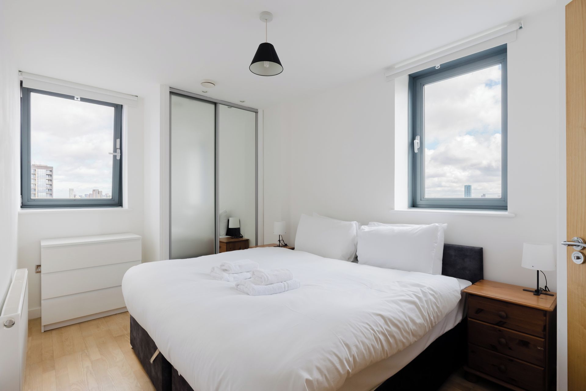 Camera da letto moderna con un letto grande, due comodini, un armadio e una finestra con vista sulla città.
