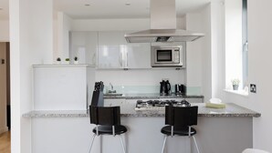 Cozinha moderna com eletrodomésticos de aço inoxidável, bancada de granito e dois banquetes pretos.