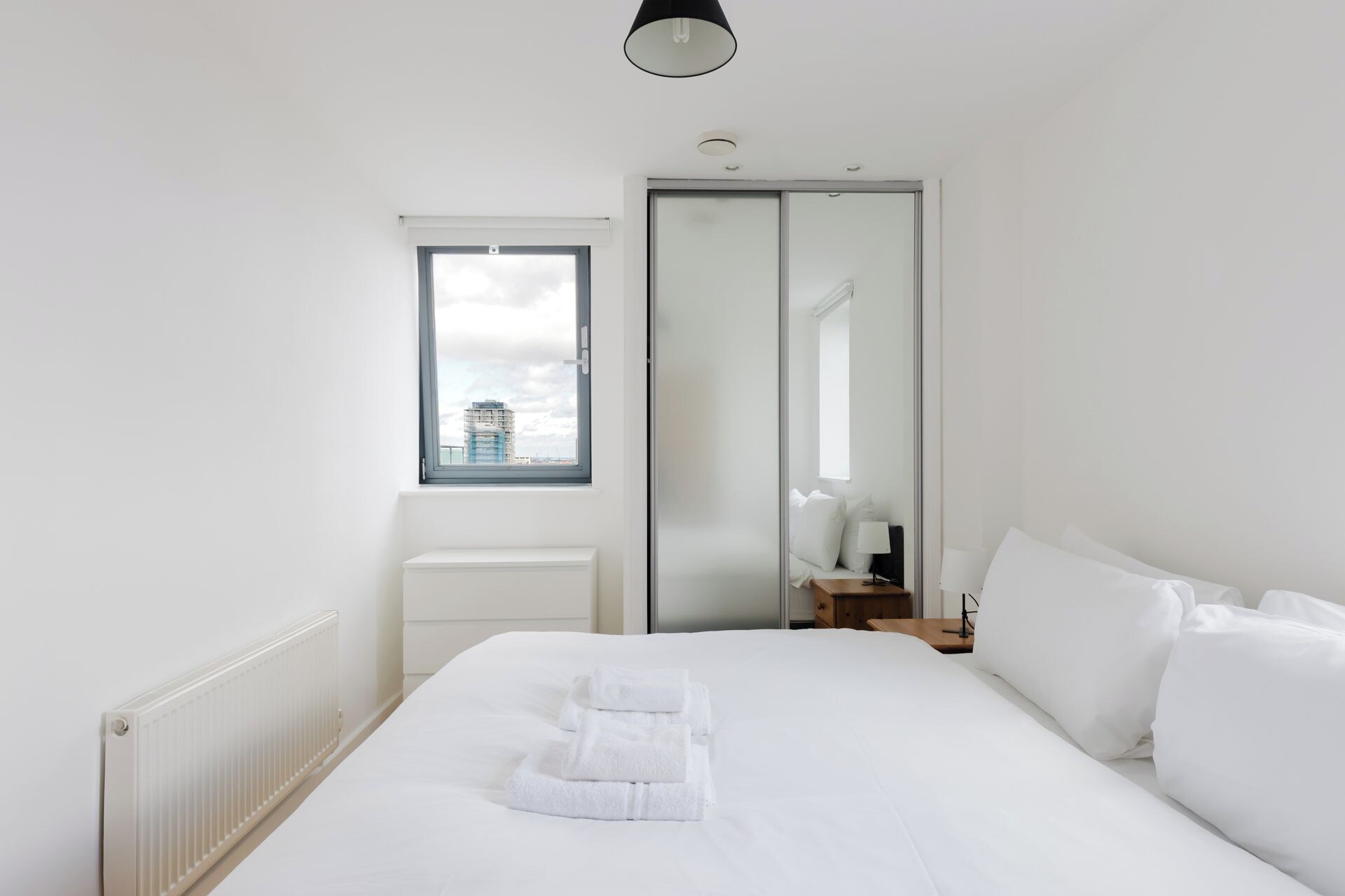 A hotel room with a bed, a window, a radiator, and a mirror.