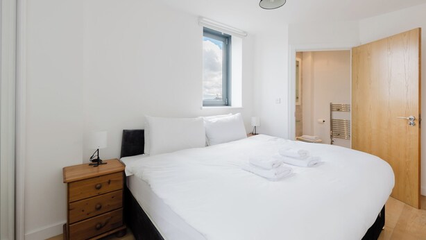 Quarto com uma cama, mesa de cabeceira, abajur, janela e porta.
