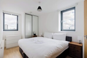 Ein Hotelzimmer mit einem Bett, Nachttischen, einem Kleiderschrank und großen Fenstern.