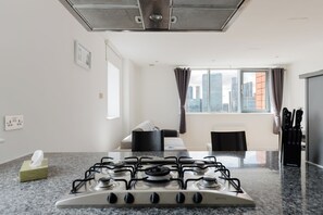 A modern kitchen with a gas stove, a window with curtains, and a view of the city skyline. - 2BDR Flat with Skyline Views in East London (Greater London)