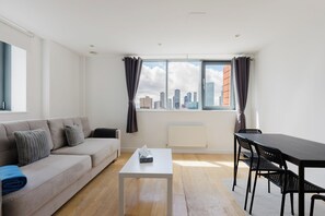 Ein modernes Wohnzimmer mit einer Couch, einem Couchtisch, einem Esstisch mit Stühlen und einem großen Fenster mit Vorhängen.