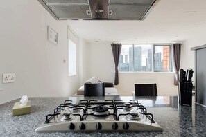 A modern kitchen with a gas stove, a window with a city view, and a dining area with a table and chairs. - 2BDR Flat with Skyline Views in East London (Greater London)