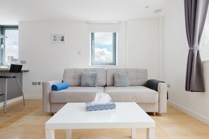 A modern living room with a sofa, a coffee table, and a window. - 2BDR Flat with Skyline Views in East London (Greater London)