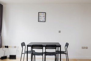 Une pièce avec une table et quatre chaises, une prise de courant et un tableau encadré au mur.