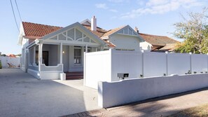 Une maison à deux étages, avec une façade blanche, un porche et un toit recouvert de tuiles rouges.