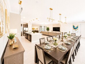 A modern kitchen with a central island, a dining area with a long table set for six, and a living area with a sofa and TV. - 27BR Grand Luxury Villas  Two Side-by-Side Homes Near Disney (Kissimmee)