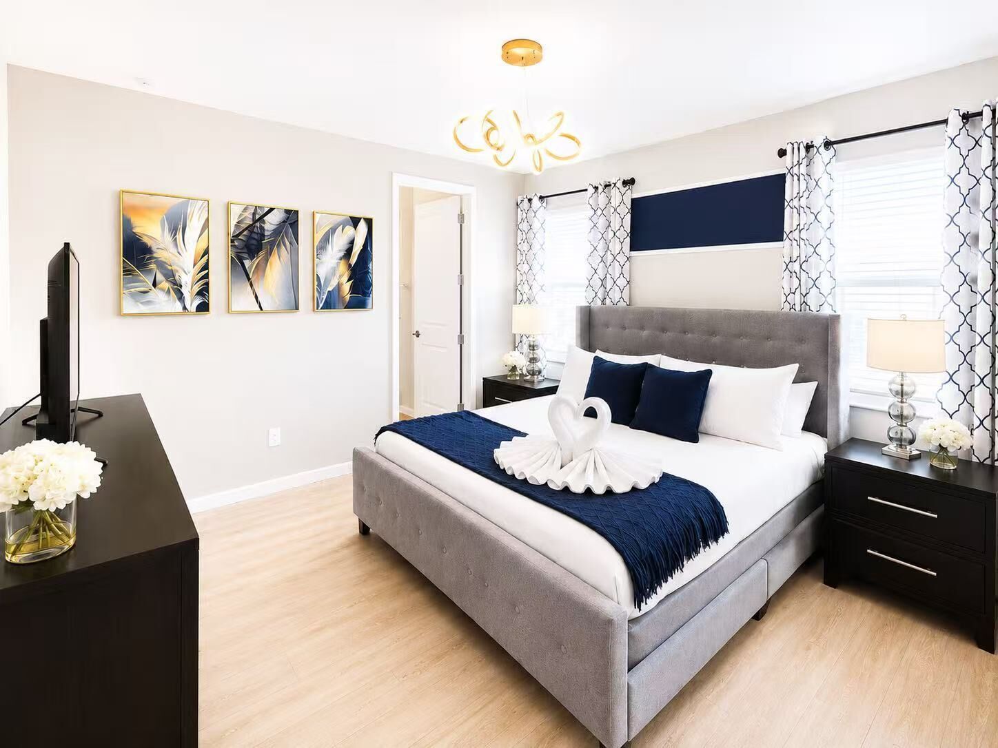 Un dormitorio moderno con una cama tapizada en gris, un televisor de pantalla plana y una obra de arte en la pared.