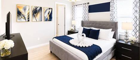 Un dormitorio moderno con una cama tapizada en gris, un televisor de pantalla plana y una obra de arte en la pared.