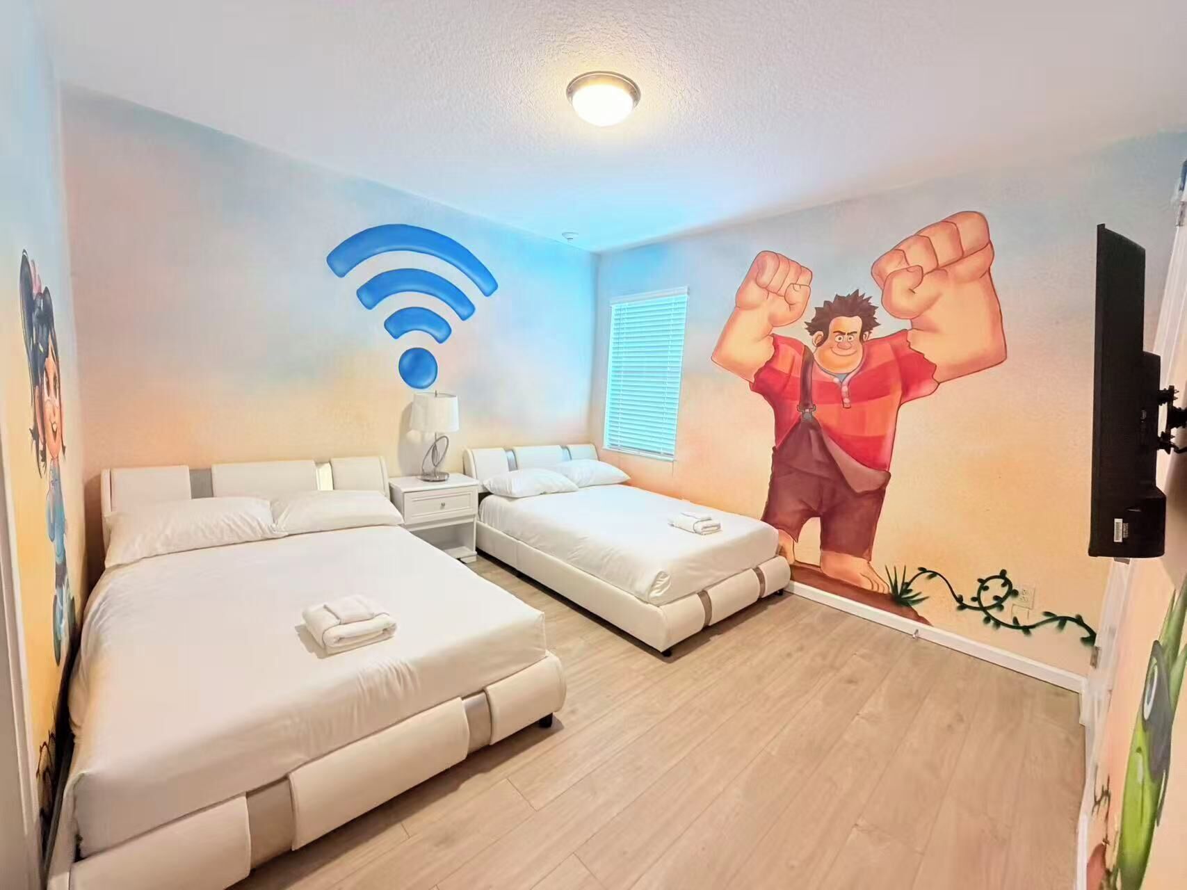 A hotel room with two beds, a nightstand, a lamp, a wall-mounted TV, and a Wi-Fi symbol.