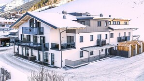 A modern multi-story building with large windows, a balcony, and a snow-covered landscape in the background. - Ski-in, ski-out in Alpine style and sauna (Hinterglemm)