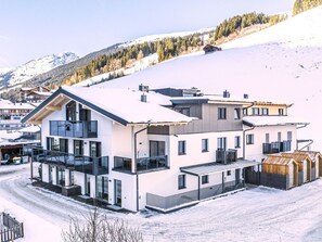 Ein modernes, mehrstöckiges Gebäude mit großen Fenstern, einem Balkon und einer verschneiten Landschaft im Hintergrund.
