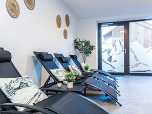 Ein moderner Wellnessraum mit Liegesesseln, einem kleinen Tisch mit Pflanzen und einem großen Fenster mit Blick auf ein Gebäude.