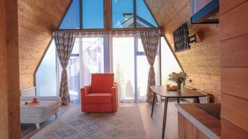 A cozy room with a wooden ceiling, a red chair, a small table with a vase, and a patterned rug.