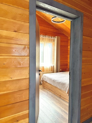 Habitació de fusta amb llit, radiador i finestra amb cortines.