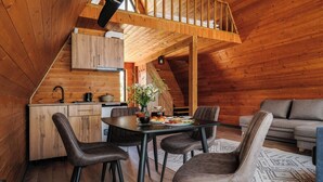 A cozy wooden interior with a dining area, kitchen, and a loft bedroom.