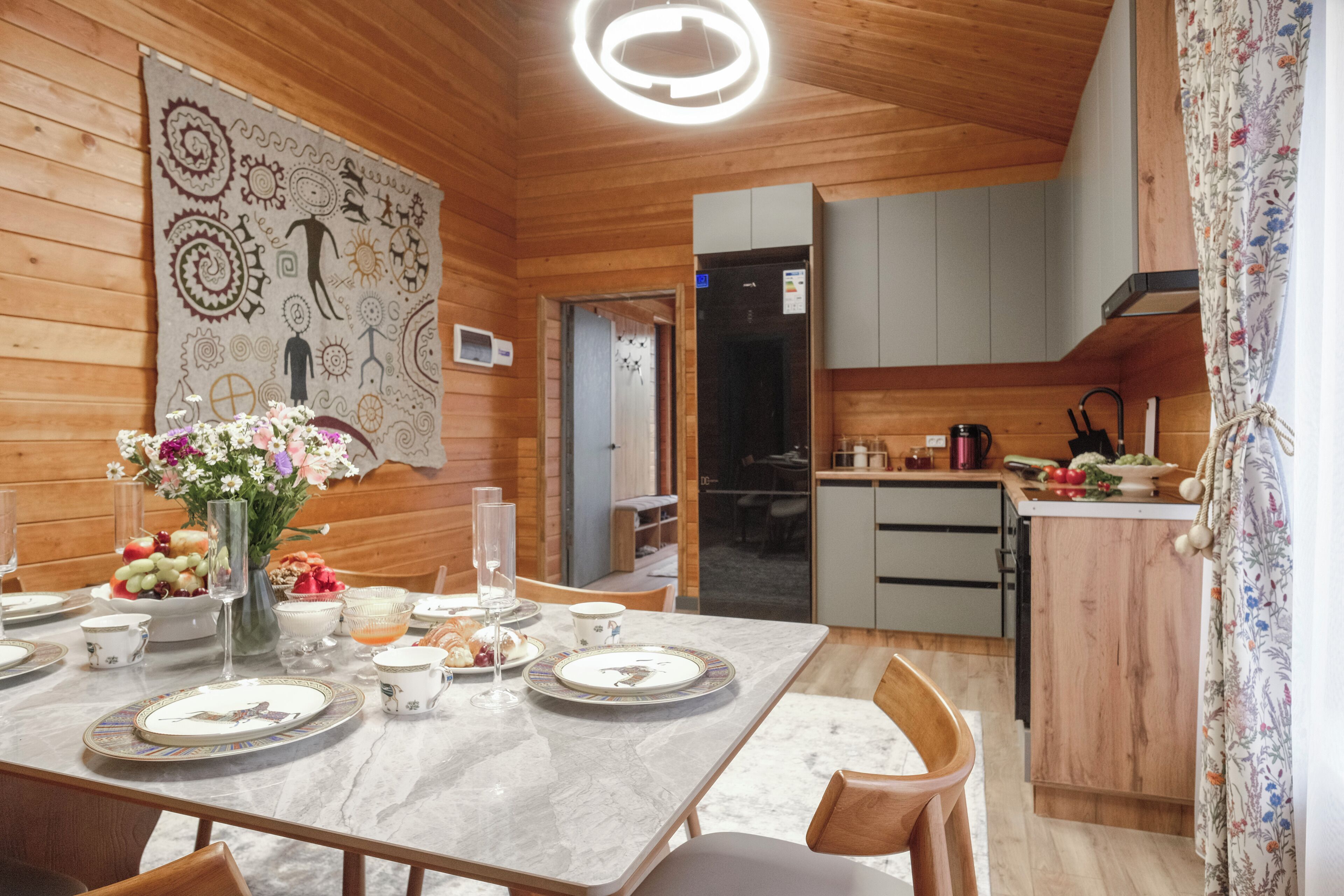 Ambiente interno in legno con un tavolo da pranzo per quattro persone, angolo cottura e un'ampia opera d'arte astratta a parete.