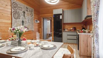 Ambiente interno in legno con un tavolo da pranzo per quattro persone, angolo cottura e un'ampia opera d'arte astratta a parete.