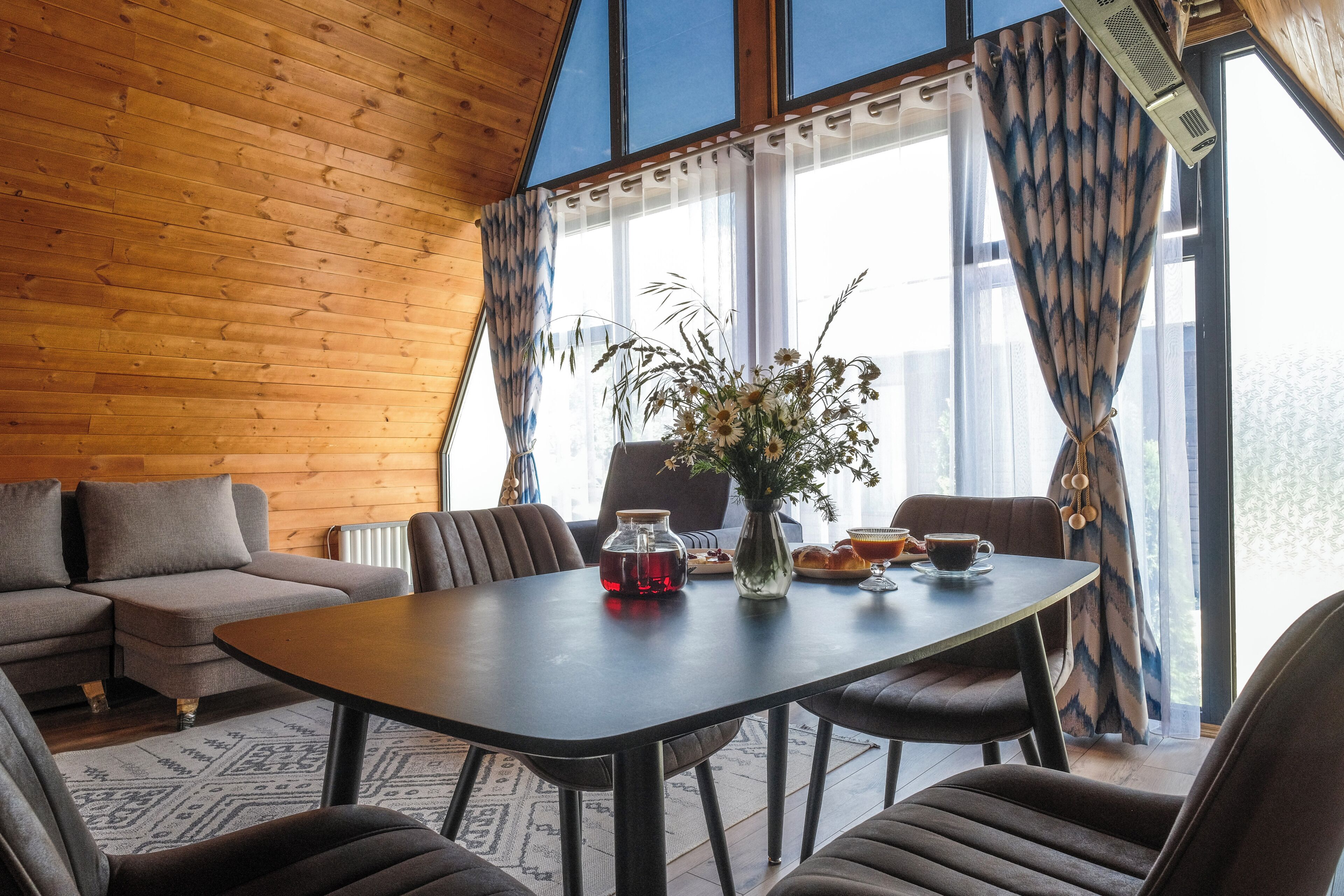 Una habitación acogedora con techo de madera, una mesa de comedor con sillas, un sofá y una ventana con cortinas.