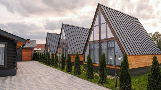 A modern building with a geometric roof design, a paved walkway, and neatly trimmed hedges.