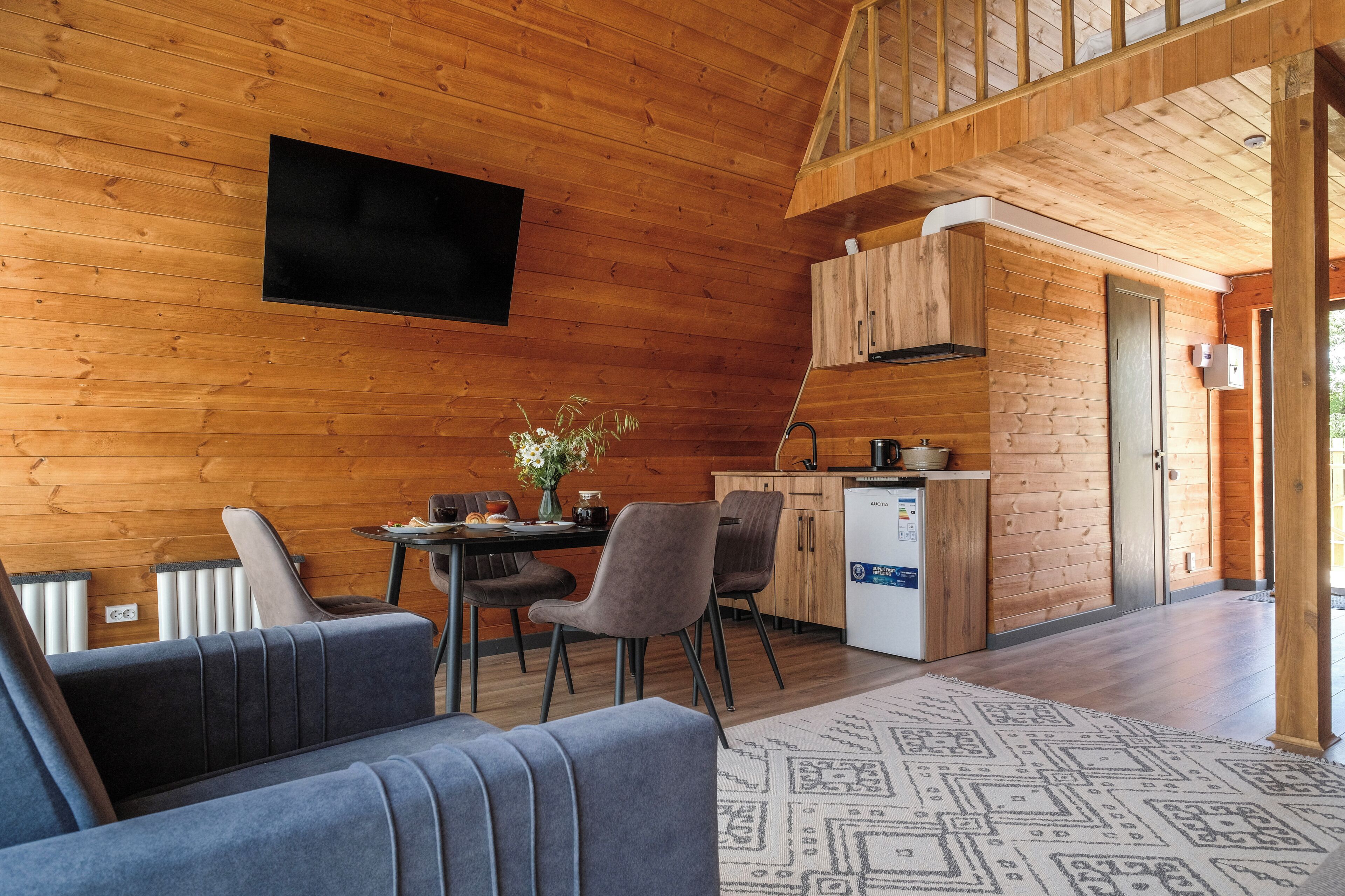A wooden cabin interior with a dining area, kitchen, and a sofa.