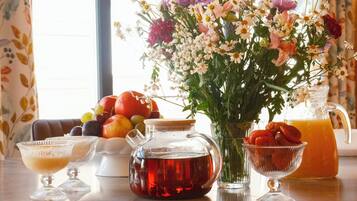 Una mesa con una jarra de té, un vaso de jarra, un cuenco de fruta y un jarrón de flores.