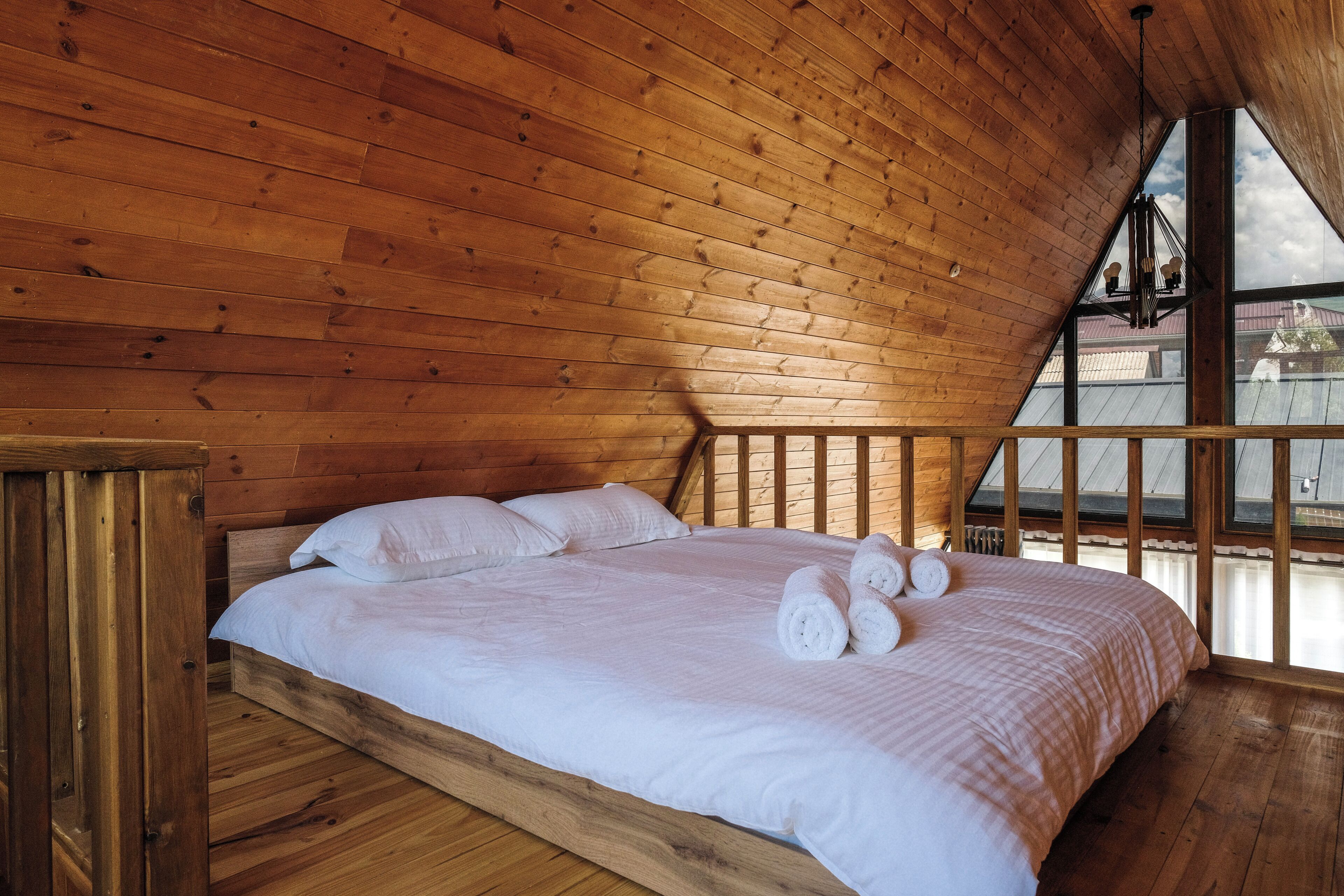 A wooden-paneled room with a bed, a window, and a view of buildings outside.