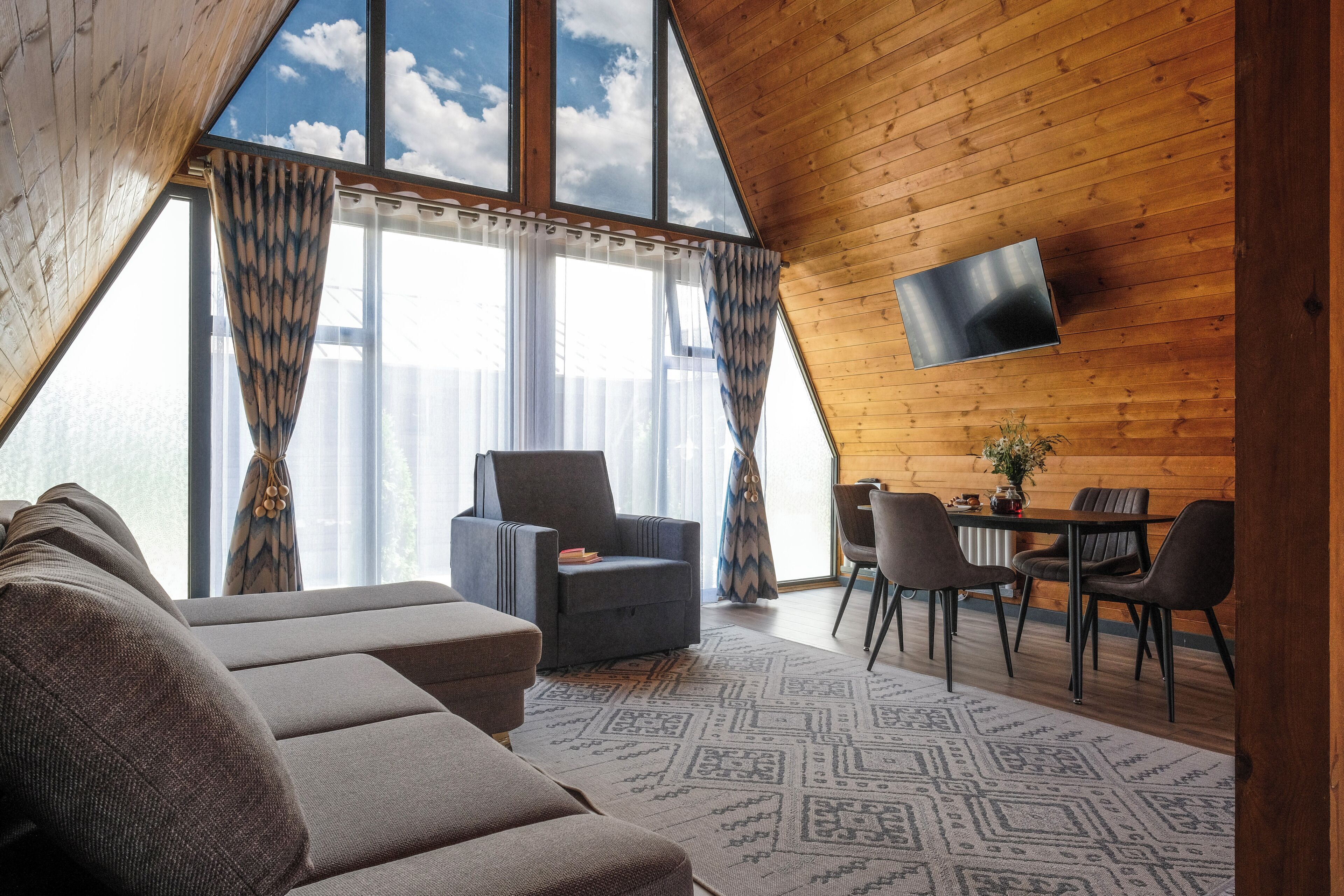 A cozy room with a large window, a flat-screen TV, a sofa, a chair, and a dining table.