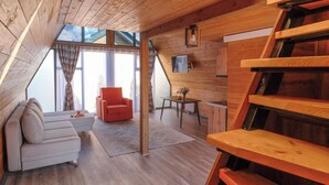 A wooden interior with a sofa, red chair, table, and a wooden staircase.