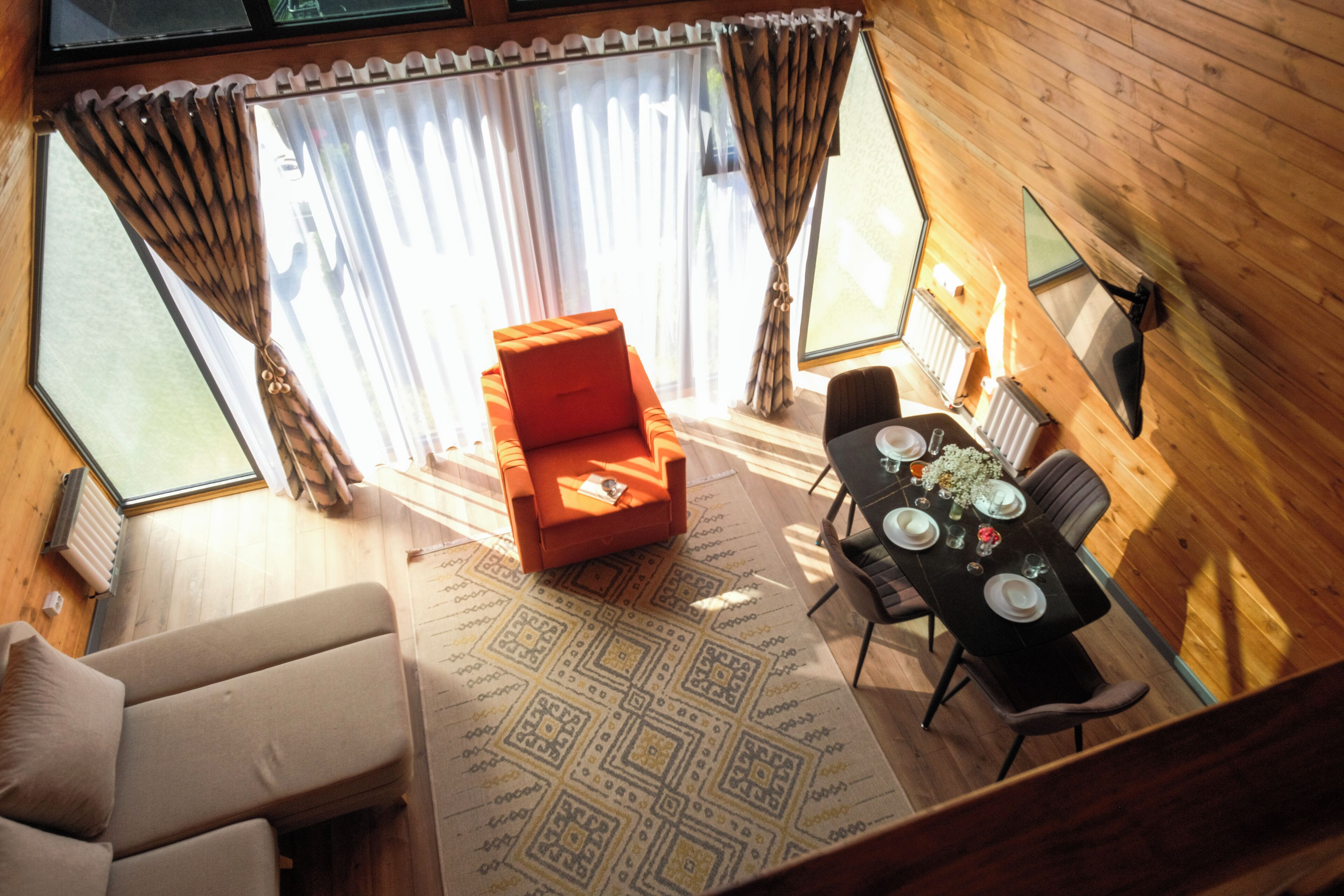 Una habitación con sofá, una mesa de comedor preparada para cuatro personas, una pequeña silla naranja y una ventana con cortinas.