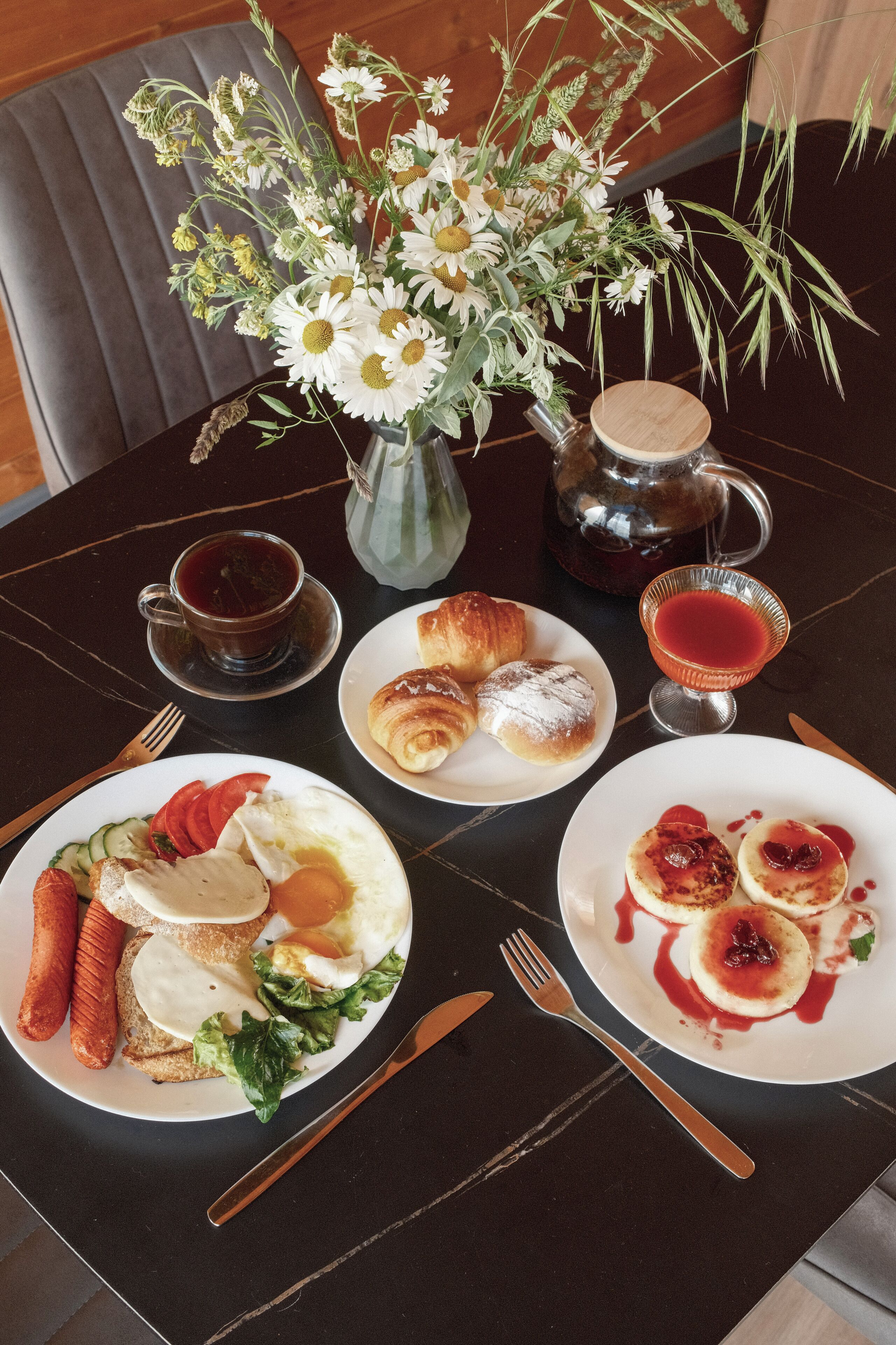 Ein Tisch mit Frühstücksangeboten, einem Blumenstrauß und einem Teekessel.