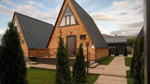 A wooden cabin with a triangular roof, a wooden deck, and a small garden area.