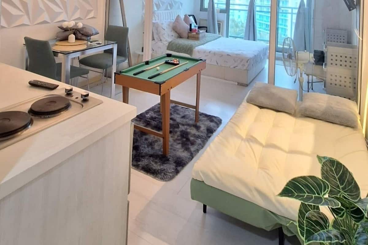 Una habitación de hotel moderna con mesa de billar, cama, escritorio con silla y un amplio ventanal con cortinas.