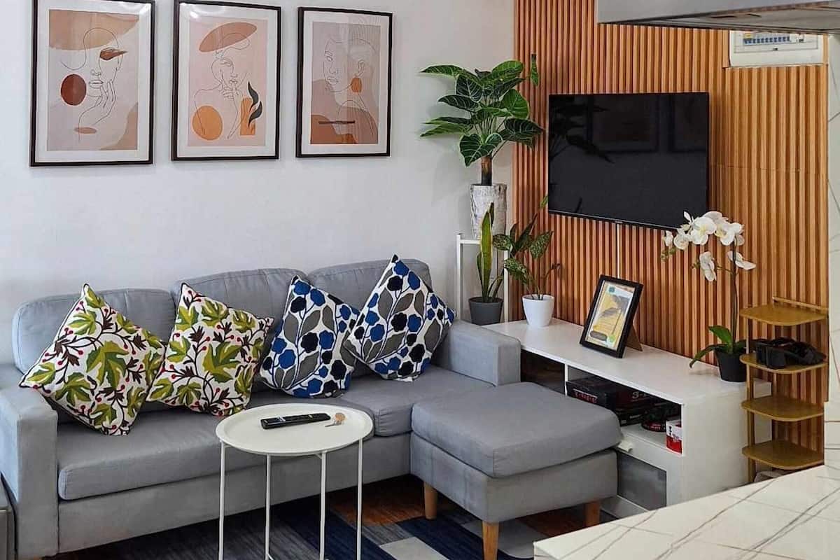 Una sala de estar moderna con un sofá gris, un televisor de pantalla plana, obras de arte enmarcadas y una planta en maceta.