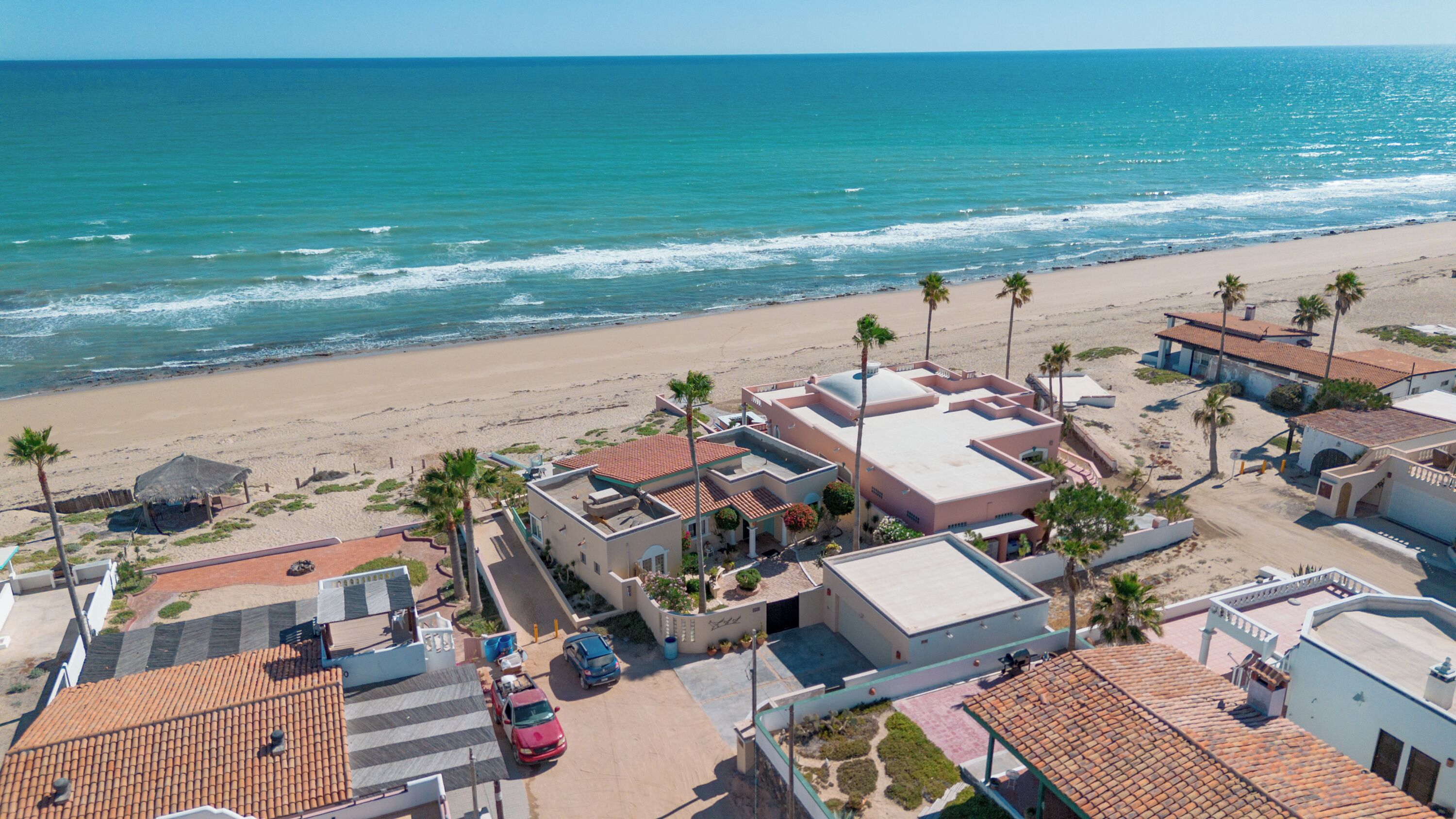 A coastal hotel with a beach view, multiple buildings, and parked cars.