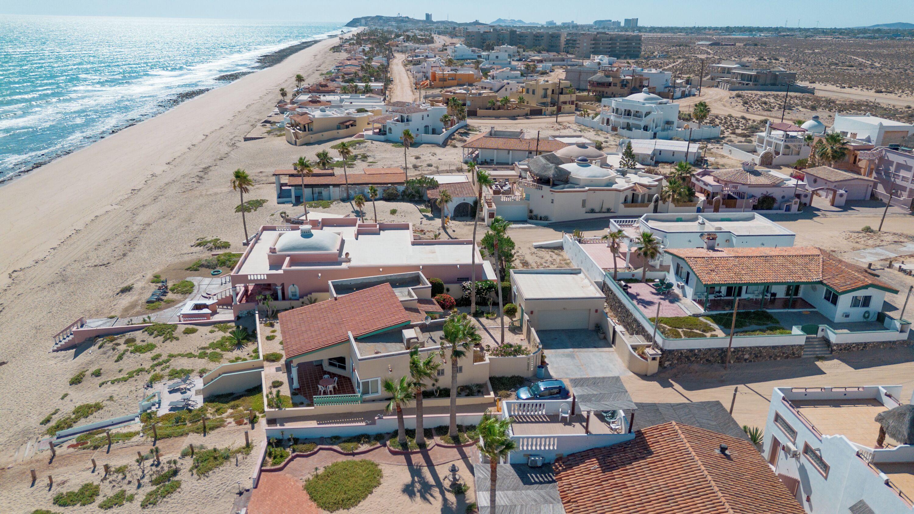 An aerial view of a coastal residential area with houses, a beach, and a clear sky.