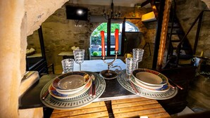 Une table à manger rustique, avec des assiettes et des verres, un lustre et une arche en pierre.