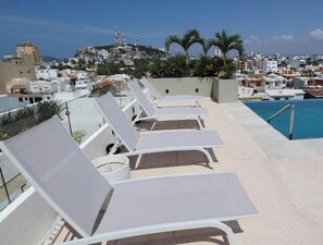 A rooftop pool area with lounge chairs and a view of a cityscape. - Modern 2BR Antara condo - Rooftop pool- Olas Altas (Mazatlán)
