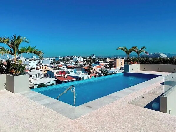 A rooftop pool with a view of a cityscape, palm trees, and a clear sky. - Modern 2BR Antara condo - Rooftop pool- Olas Altas (Mazatlán)