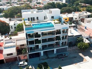 Ein mehrstöckiges Gebäude mit Pool auf dem Dach, Balkonen mit Bepflanzung und Blick auf die Straße.