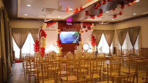 A conference room with rows of wooden chairs, a stage with a large screen, and red and white balloons.