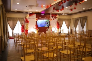 A conference room with rows of wooden chairs, a stage with a large screen, and red and white balloons.