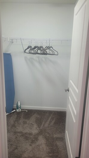 Quarto com piso coberto por carpete, um varal de roupas e um objeto azul à esquerda.