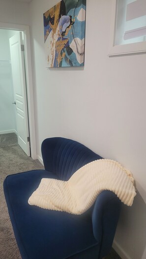 Um quarto com uma poltrona azul, uma porta branca e um quadro na parede.