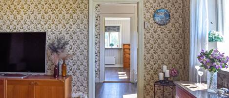A room with floral wallpaper, a television, a wooden cabinet, a small table with candles, and a window with a view.