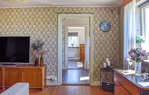 A room with floral wallpaper, a television, a wooden cabinet, a small table with candles, and a window with a view. - Awesome home in Ystad with WiFi (Ystad)