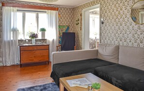 Ein Zimmer mit einem Holzkoffer, einem Sofa, einem kleinen Tisch, einem Spiegel und einem Fenster mit Vorhängen.