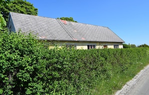 Ein Haus mit geneigtem Dach, umgeben von üppigem Grün und einem Kiesweg.
